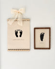 Framed black footprints on a beige background with a decorative bow.