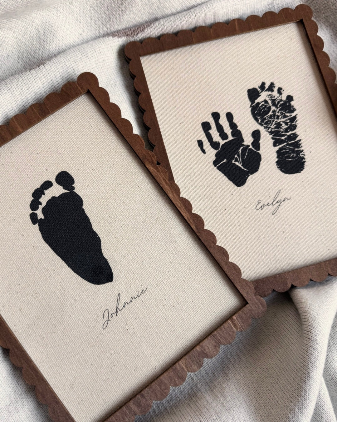Two framed prints with black hand and footprints on beige fabric backgrounds.